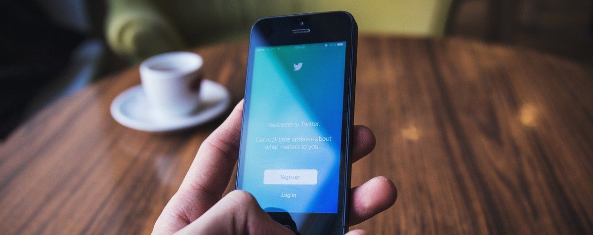 Twitter App auf Smartphone, Kaffeetasse auf Tisch im Hintergrund