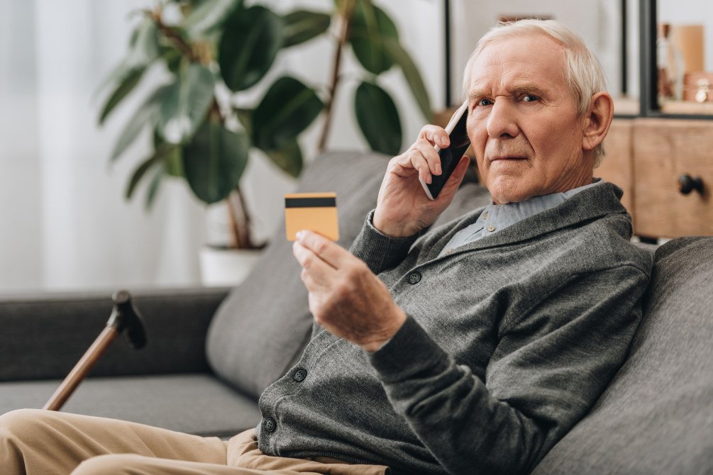 Senior spricht am Smartphone und hält Kreditkarte in der Hand